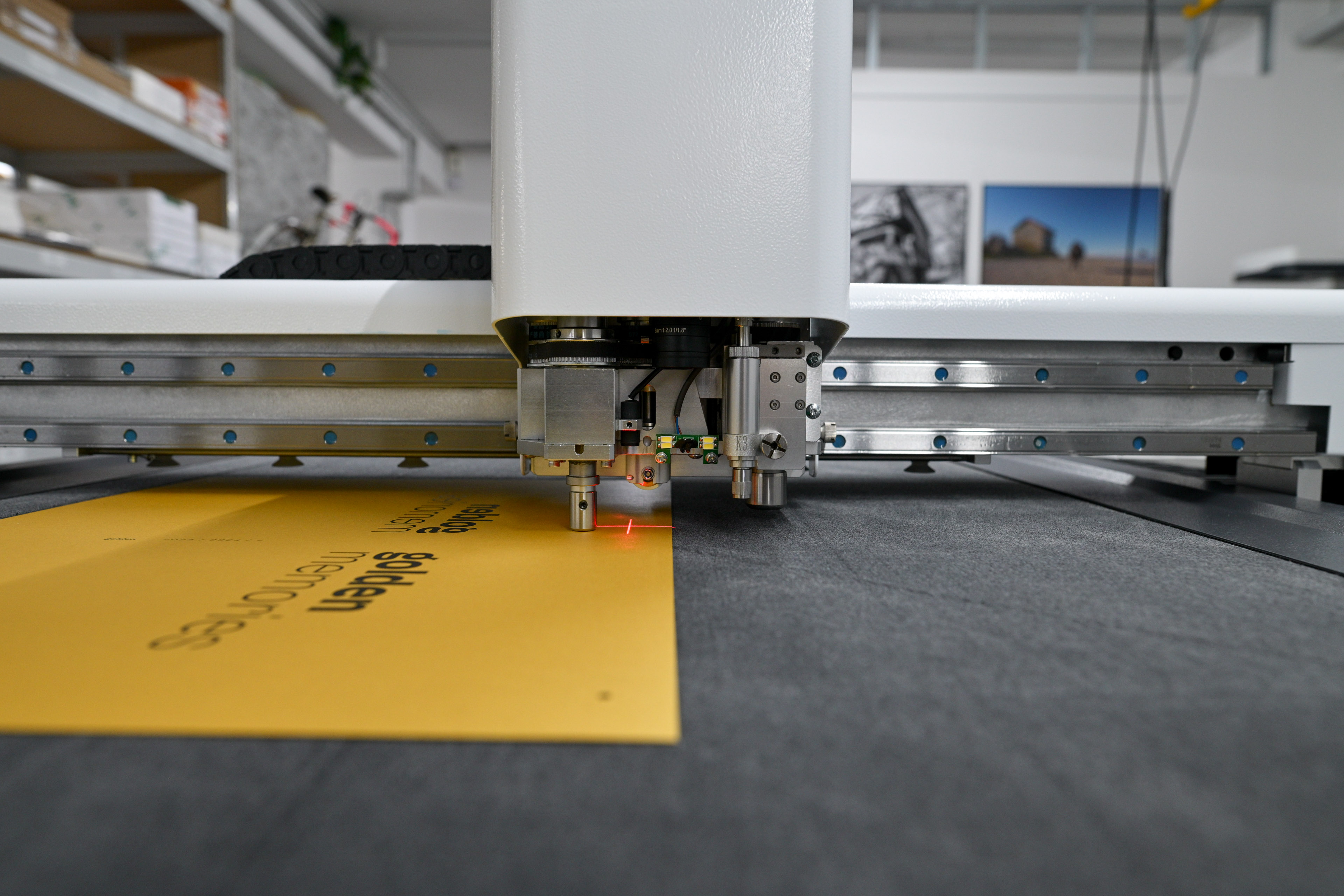 Nahaufnahme einer digitalen Schneidemaschine mit einem roten Laser, der auf einem gelben Blatt mit schwarzem Text ausgerichtet ist.
